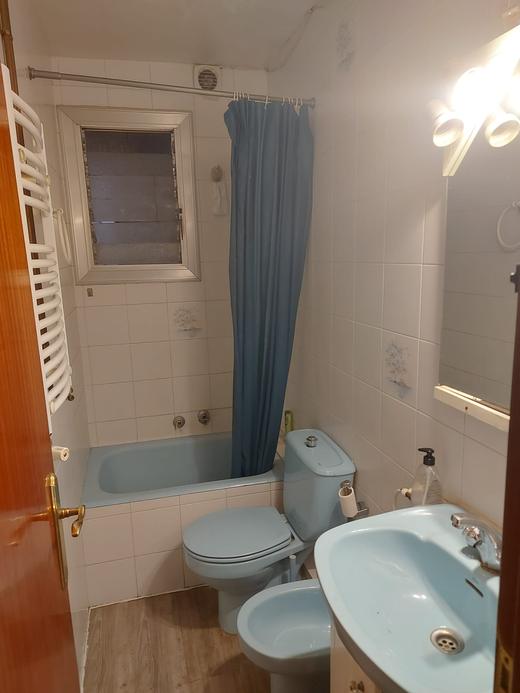 The same bathroom before the work: a bath with a curtain, a blue suite and the original white tiling