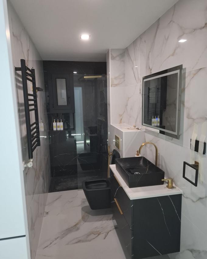 Renovated bathroom with a level-access shower, black and white marble-effect porcelain, a black basin on a wall-hung vanity and brass taps