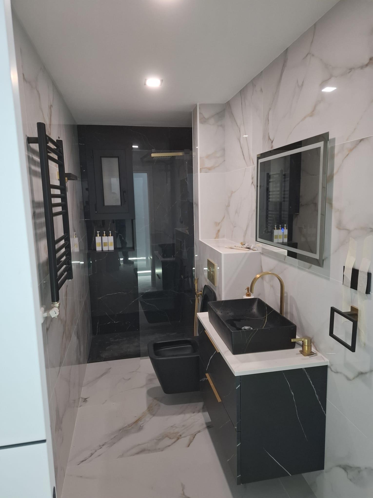 Renovated bathroom with a level-access shower, black and white marble-effect porcelain, a black basin on a wall-hung vanity and brass taps