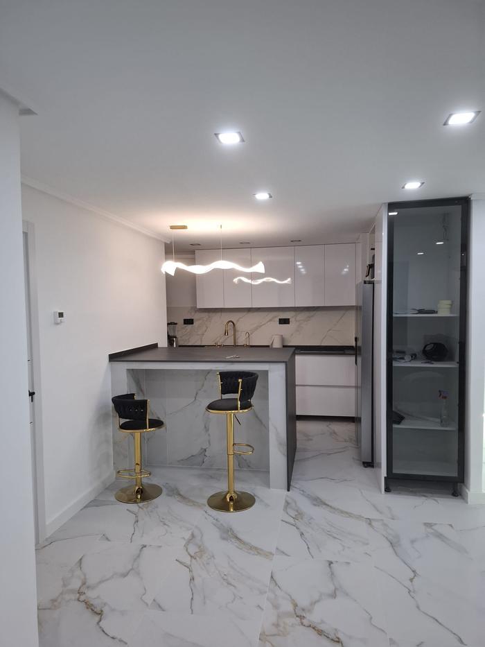 Kitchen opened onto the living room with a peninsula, bar stools, white lacquered units and a marble-effect porcelain floor