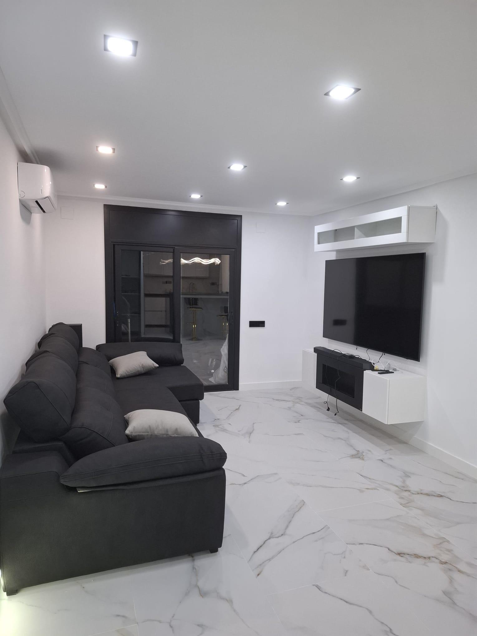 Renovated living room with a marble-effect porcelain floor, a black-framed glazed partition to the kitchen and a wall-hung media unit