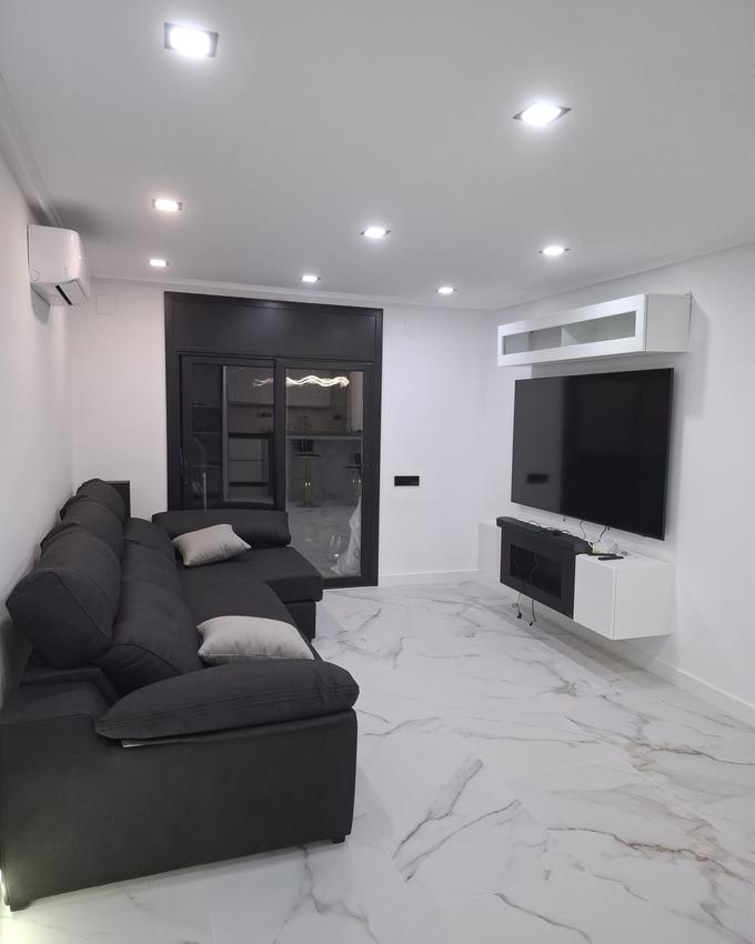 Renovated living room with a marble-effect porcelain floor, a black-framed glazed partition to the kitchen and a wall-hung media unit