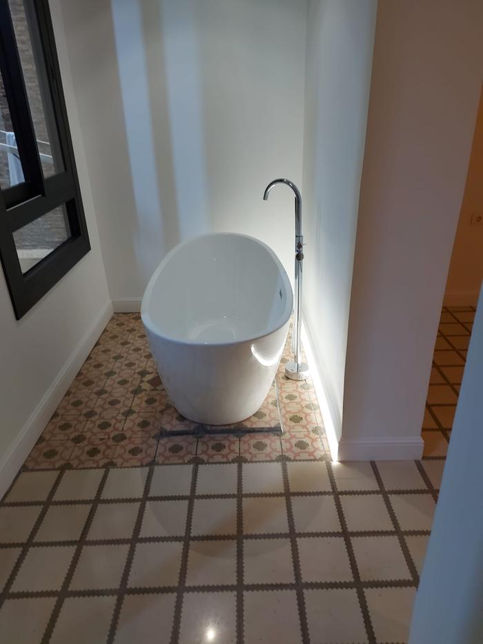 Freestanding bath set on the original hydraulic tile floor, beside a black-framed window