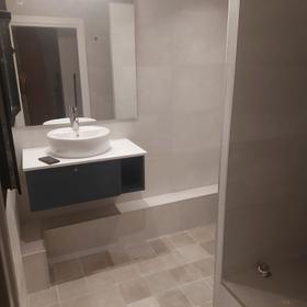 Second bathroom in the same flat, with a level-access shower, large-format grey porcelain and a round countertop basin