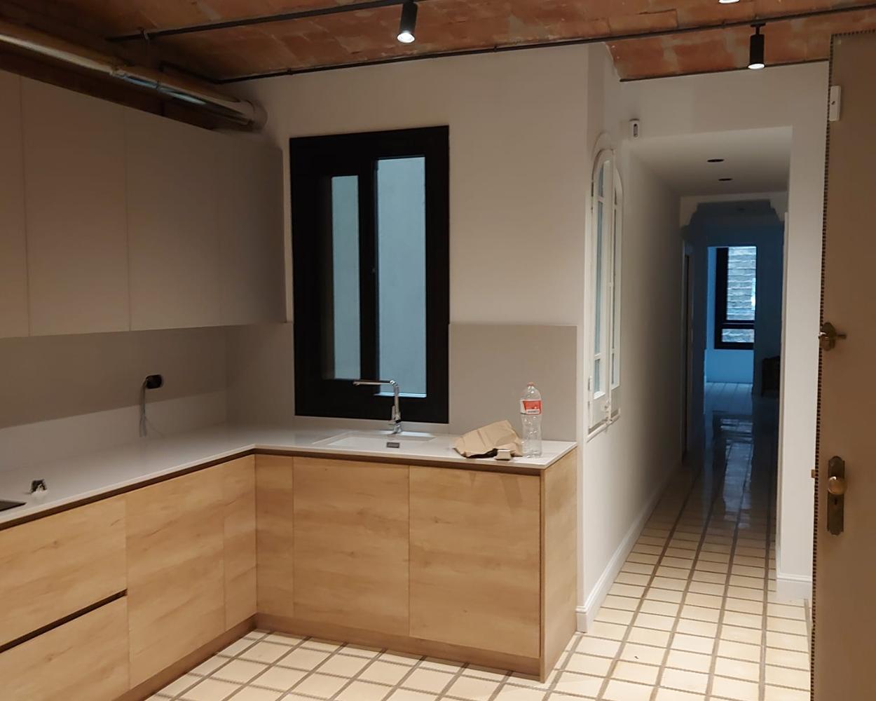 Kitchen under an exposed Catalan brick vault, with pale wood fronts, a white worktop and a black-framed window