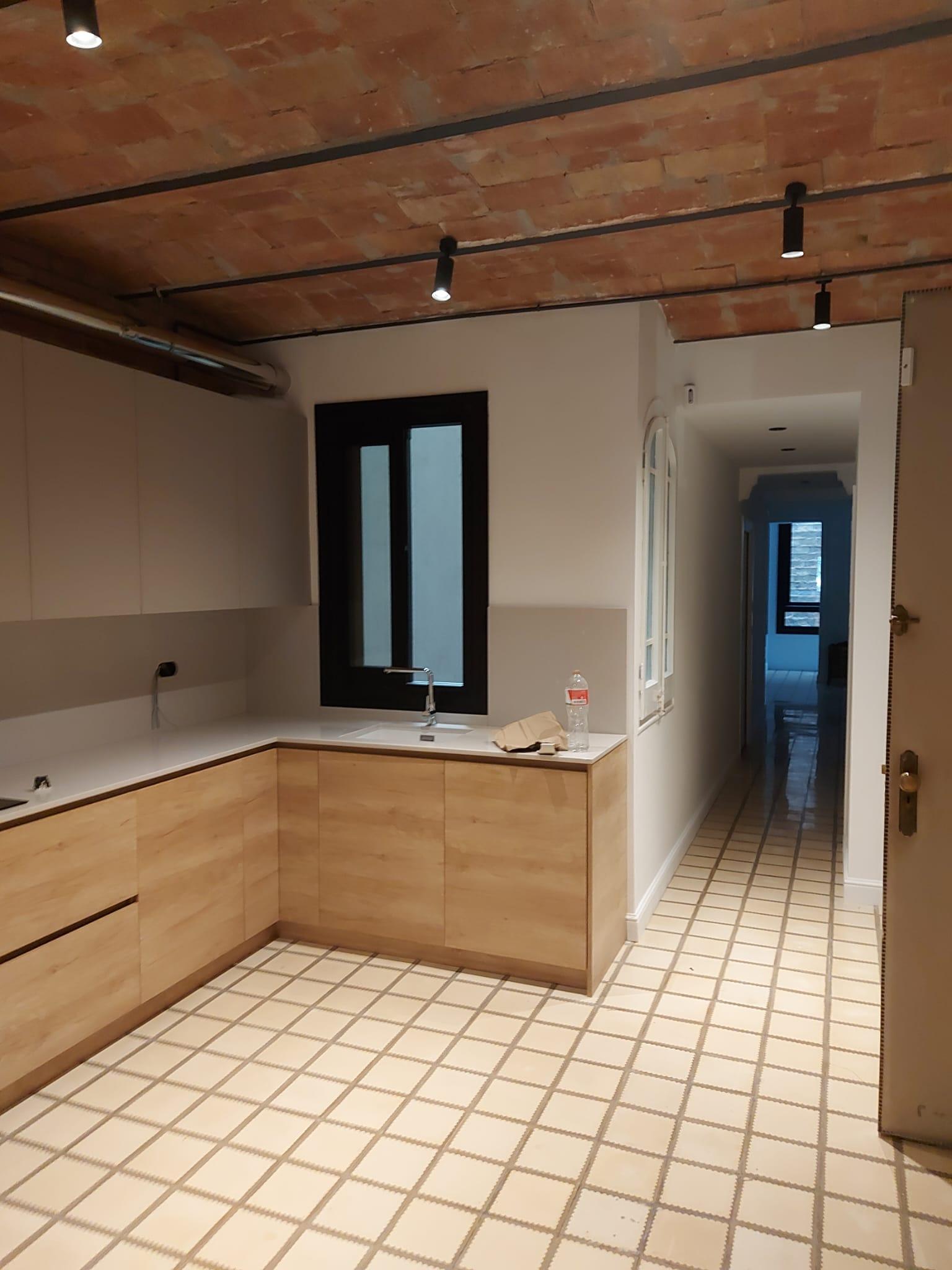 Kitchen under an exposed Catalan brick vault, with pale wood fronts, a white worktop and a black-framed window