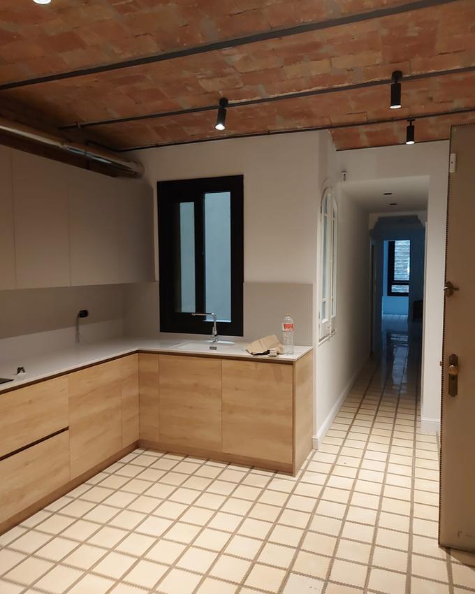 Kitchen under an exposed Catalan brick vault, with pale wood fronts, a white worktop and a black-framed window